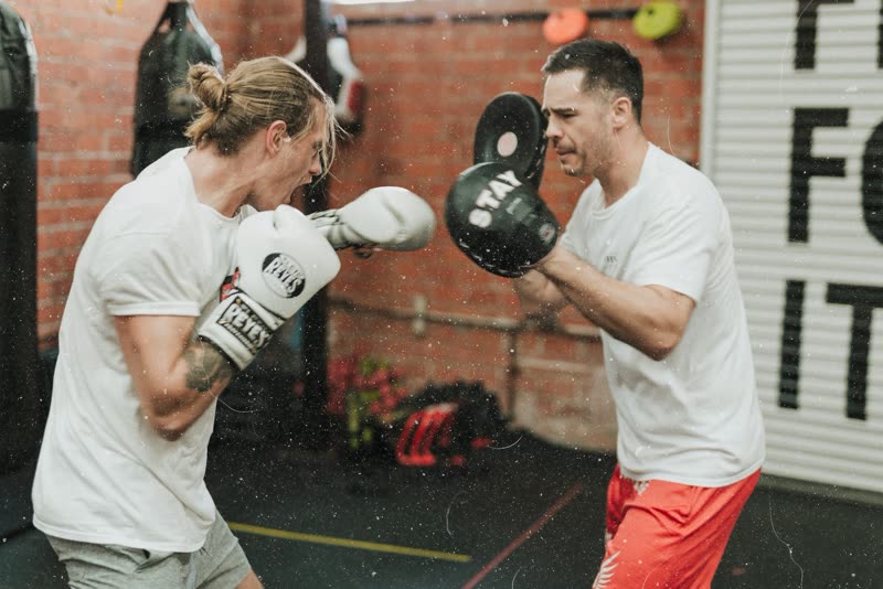 Professor segurando aparadores para o aluno treinar boxe